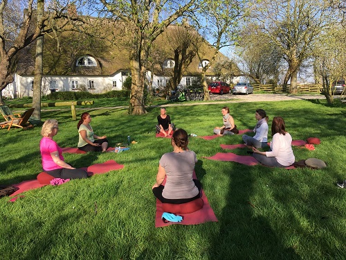 Yoga im Freien vor einem Reethaus