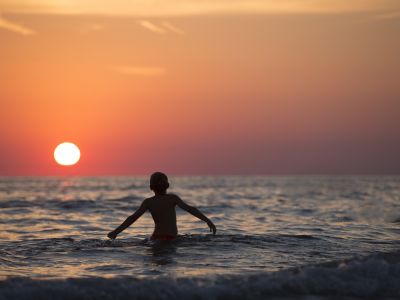 Junge badet im Meer im Sonnenuntergang